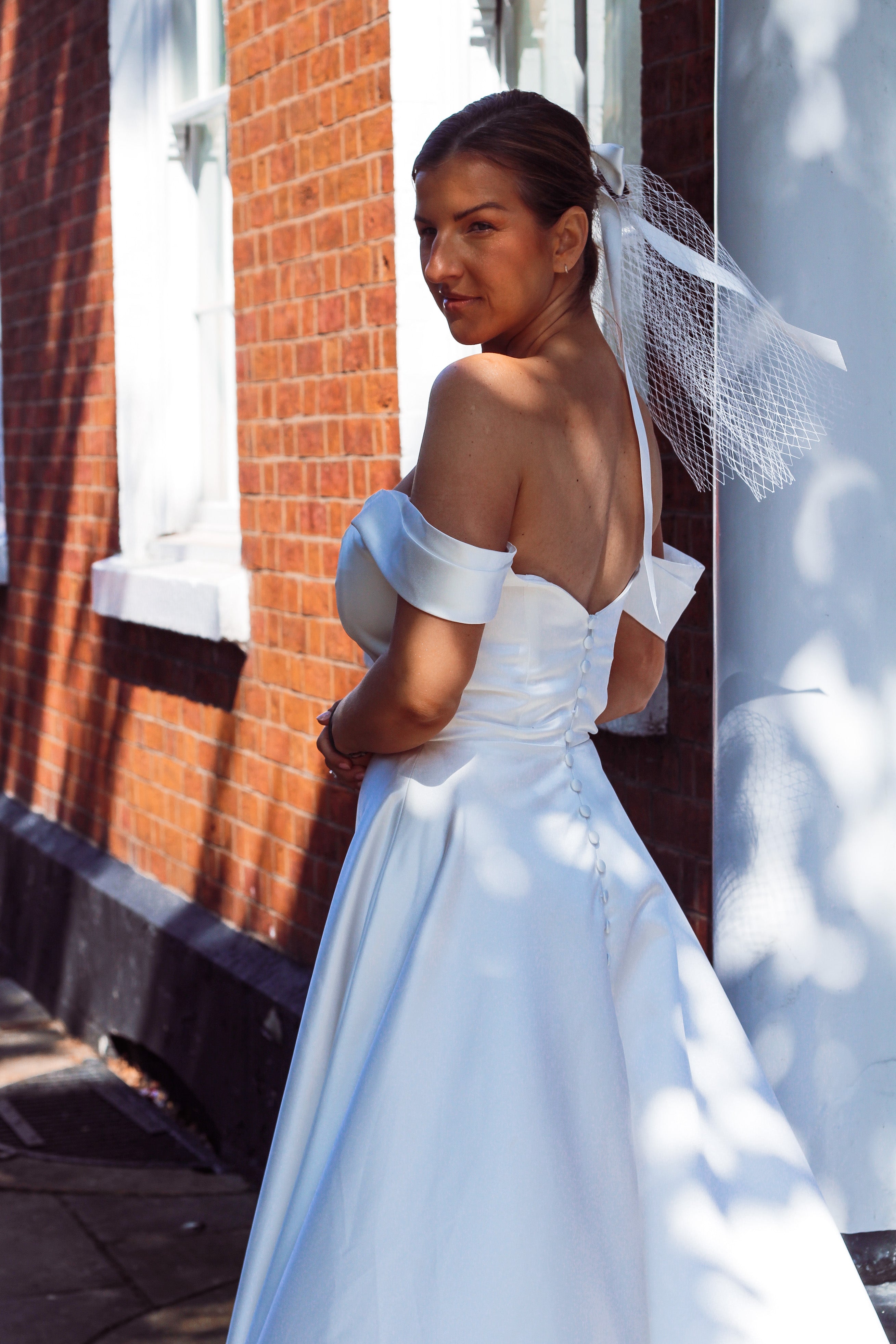 A young bride wearing Velo Bianco minimalistic off the shoulder satin wedding dress with buttoned back paired with short elegant wedding veil and white bridal heels. Manchester City hall wedding outfit for the modern bride.