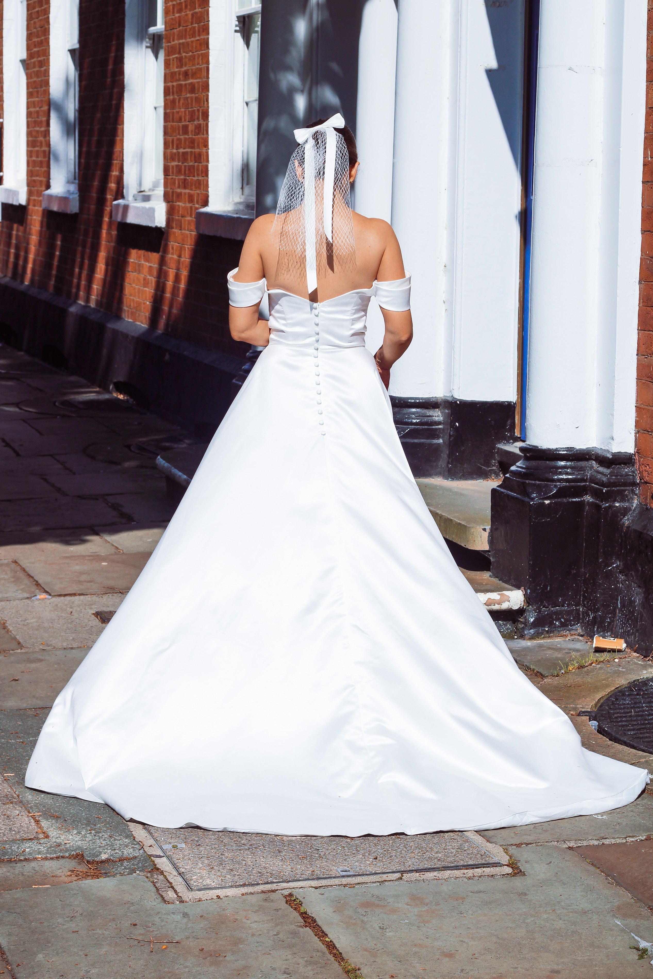 A young bride wearing Velo Bianco minimalistic off the shoulder satin wedding dress with buttoned back paired with short elegant wedding veil and white bridal heels. Manchester City hall wedding outfit for the modern bride.
