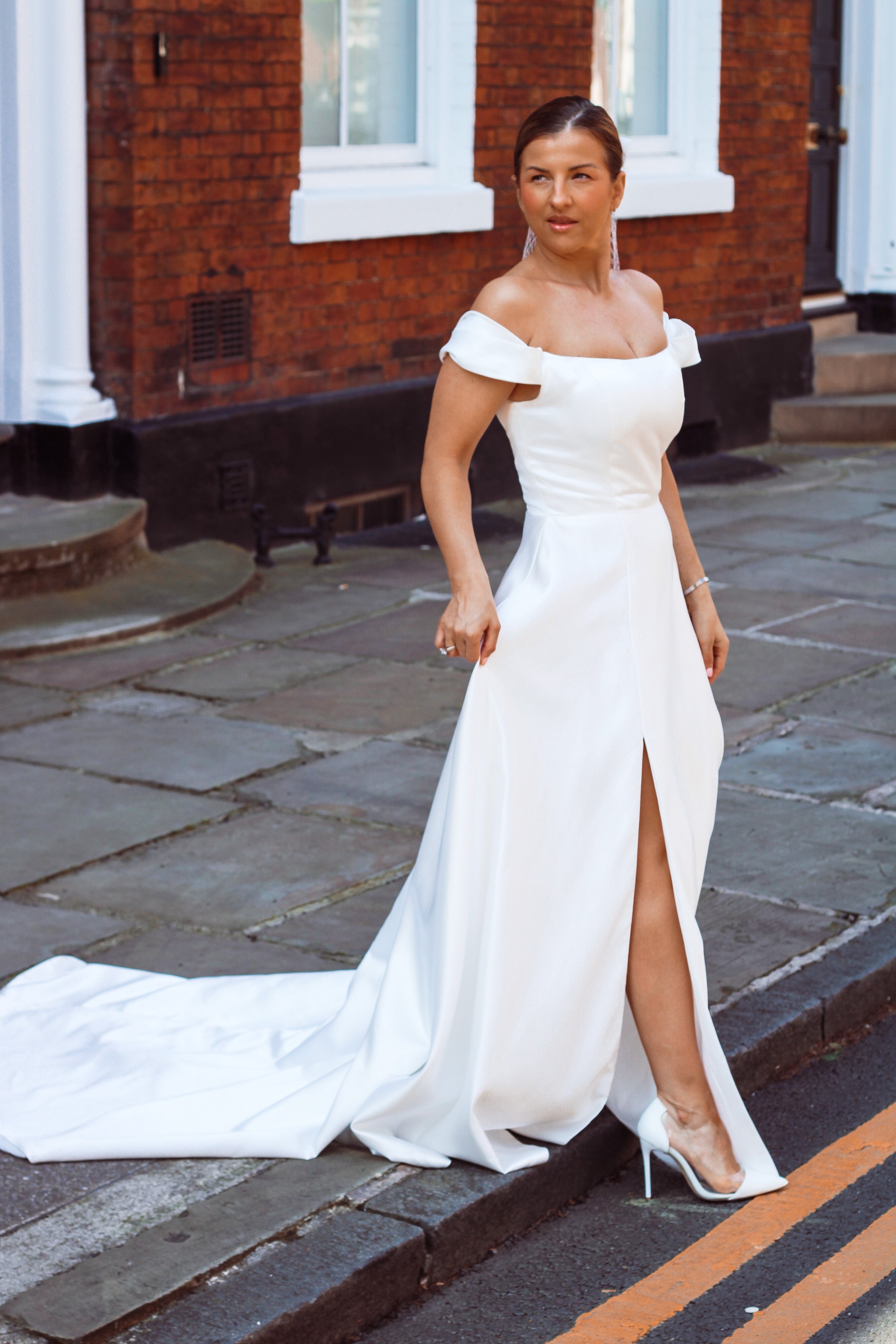 A young bride wearing Velo Bianco minimalistic off the shoulder satin wedding dress with buttoned back paired with short elegant wedding veil and white bridal heels. Manchester City hall wedding outfit for the modern bride.