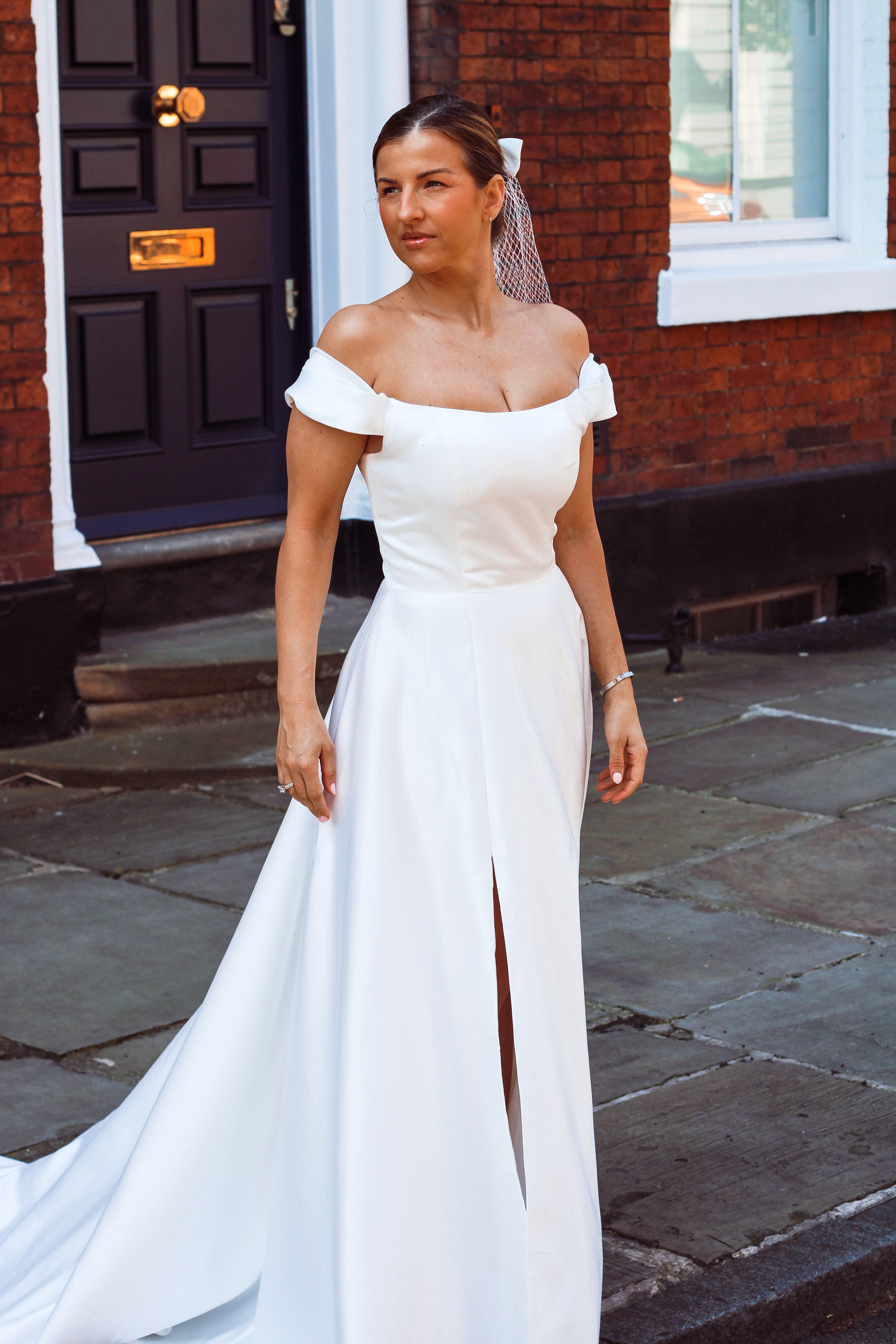 A young bride wearing Velo Bianco minimalistic off the shoulder satin wedding dress with buttoned back paired with short elegant wedding veil and white bridal heels. Manchester City hall wedding outfit for the modern bride.