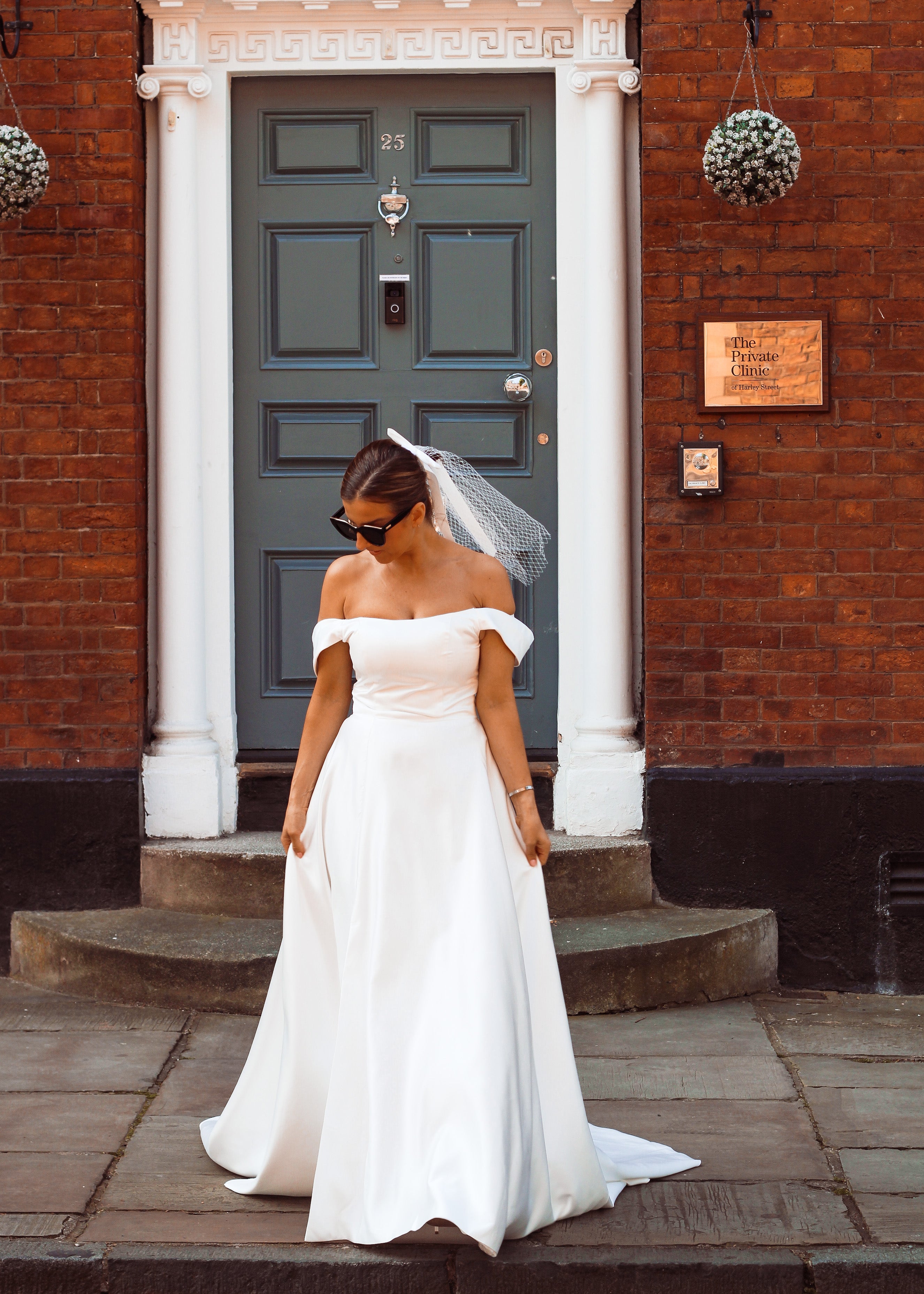 A young bride wearing Velo Bianco minimalistic off the shoulder satin wedding dress with buttoned back paired with short elegant wedding veil and white bridal heels. Manchester City hall wedding outfit for the modern bride.