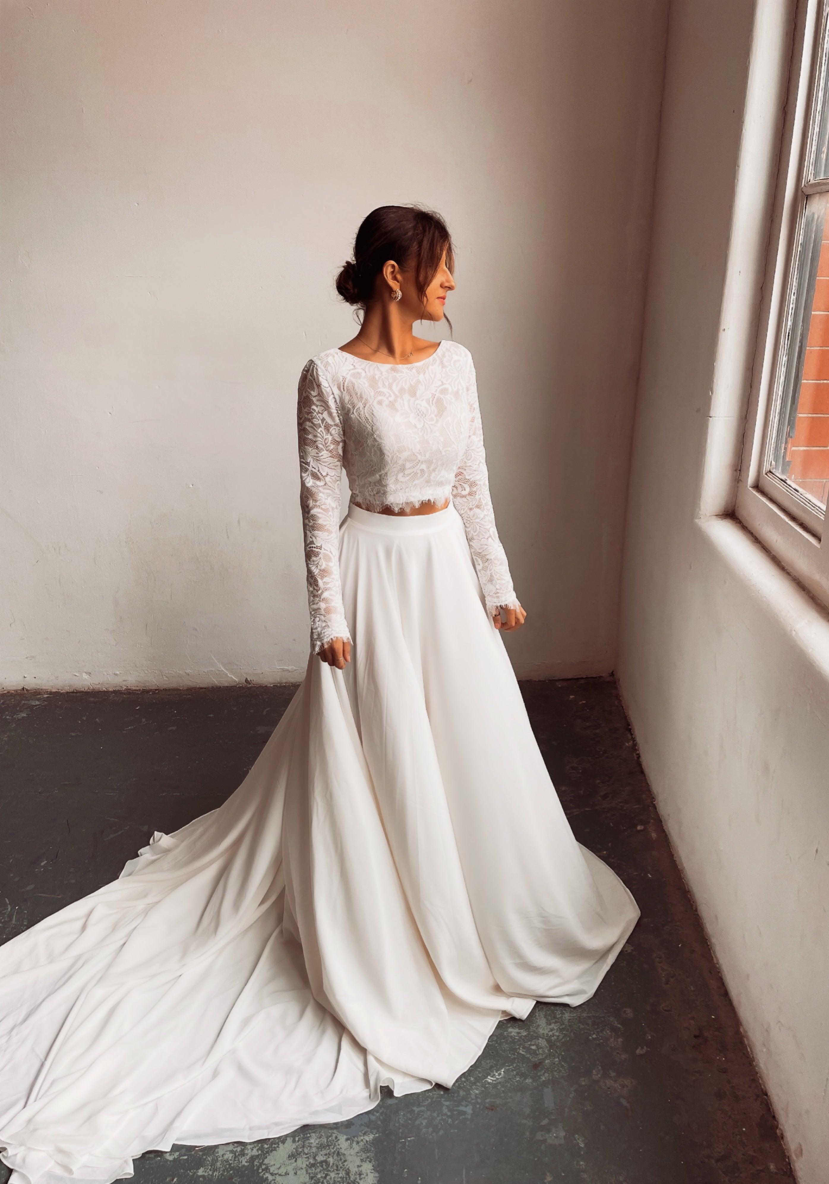 A bride wearing a two piece cream bohemian lace wedding dress. The lace top is long sleeve and the chiffon skirt is high waisted. This two piece lace dress is perfect for boho themed weddings and elopements.