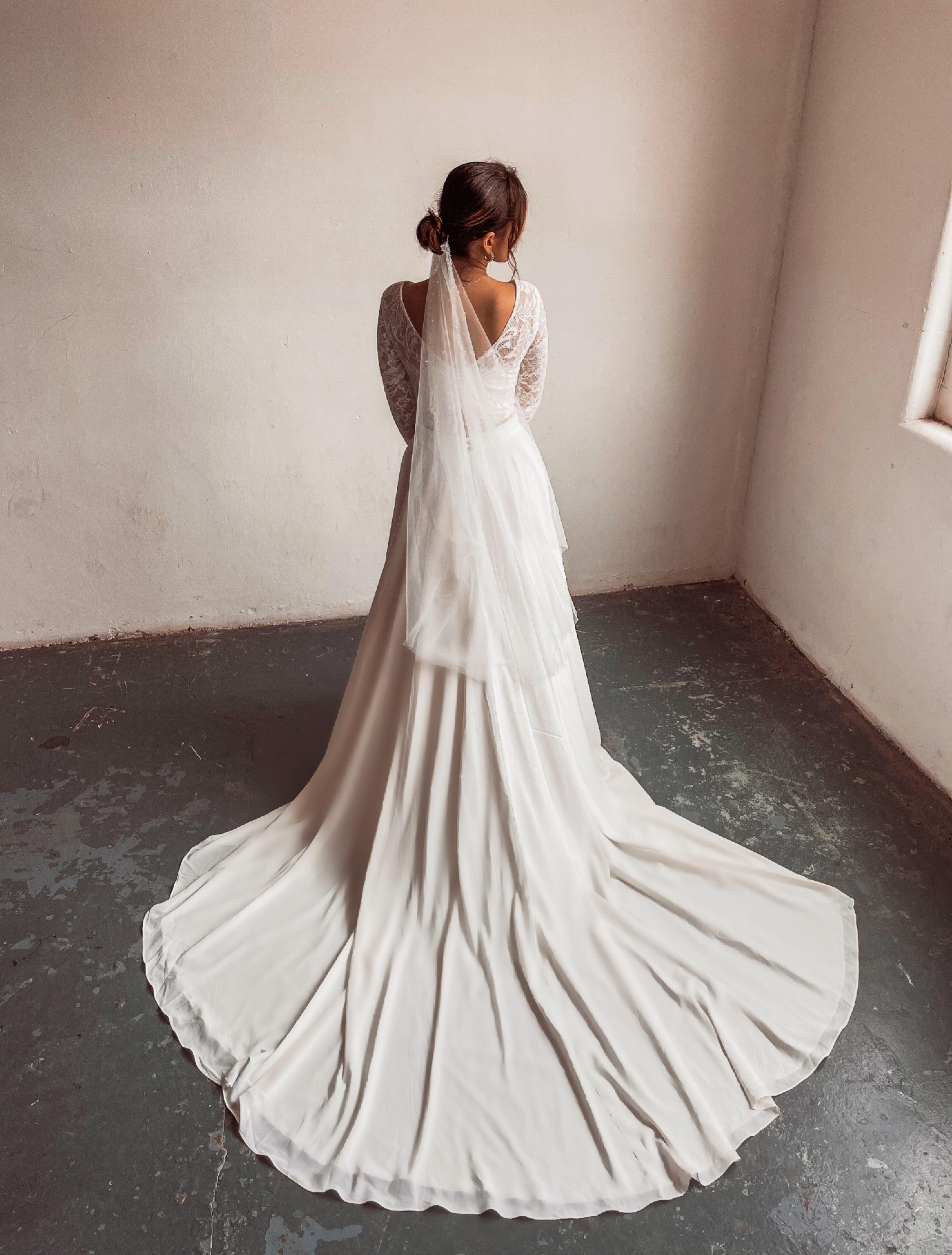 A bride wearing a two piece bohemian lace wedding dress. The ivory lace top is long sleeve and the chiffon skirt is high waisted. This two piece lace dress is perfect for boho themed weddings, rustic weddings and elopements.