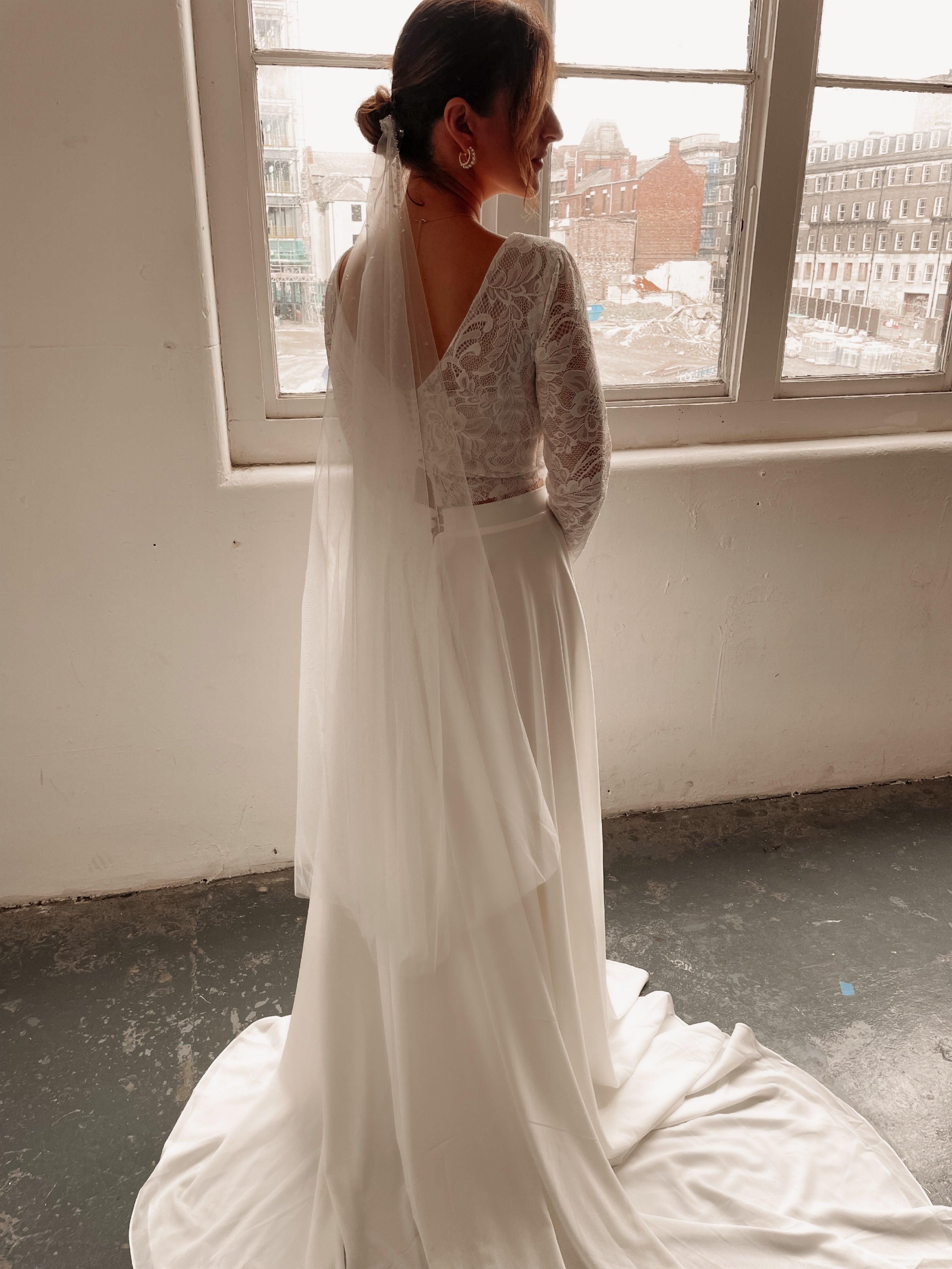 A bride wearing a two piece ivory bohemian lace wedding dress. The lace top is long sleeve and the chiffon skirt is high waisted. This two piece lace dress is perfect for boho themed weddings and elopements.