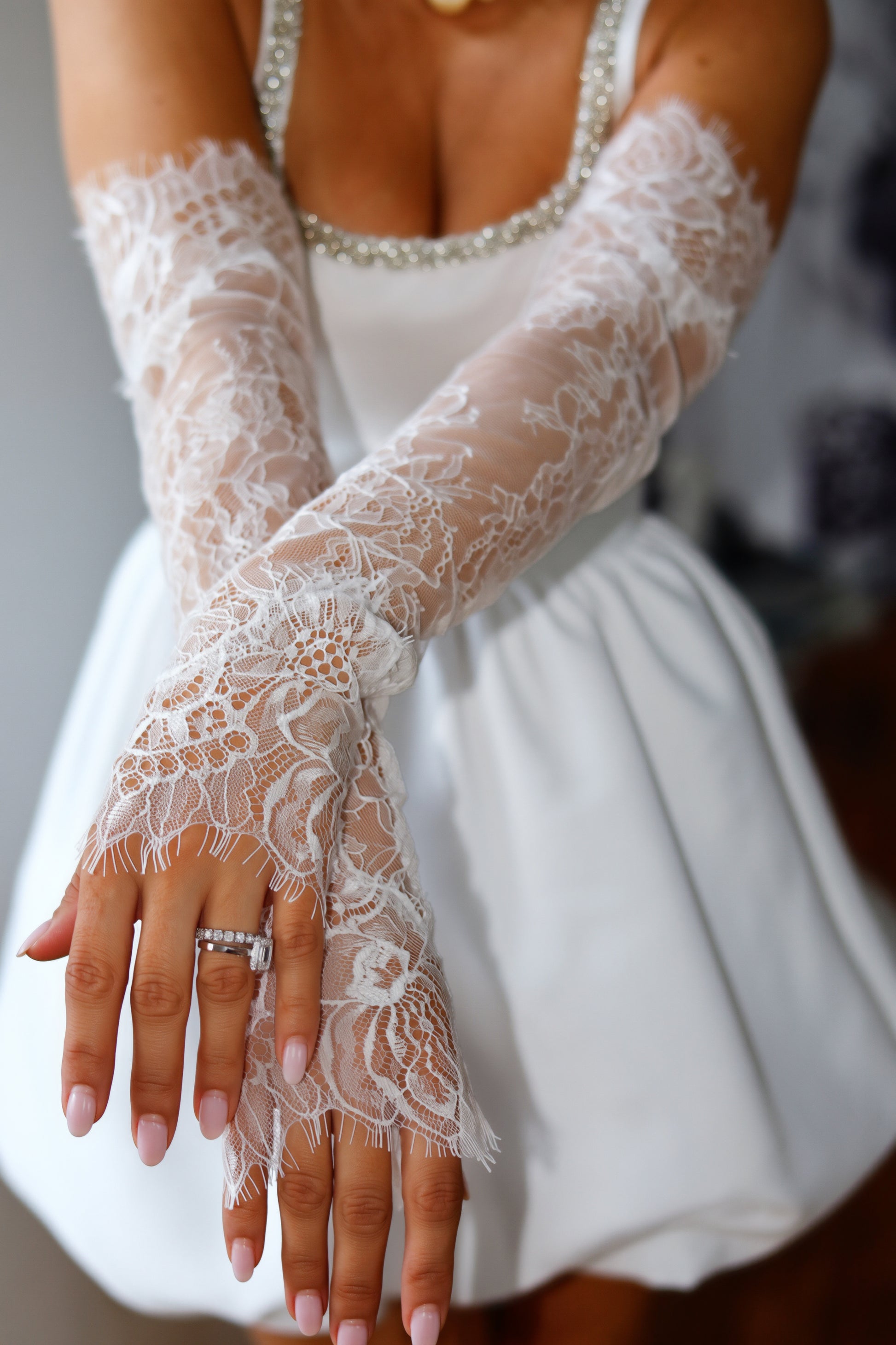 White lace bridal gloves worn on a model's arms, paired with a white wedding dress.